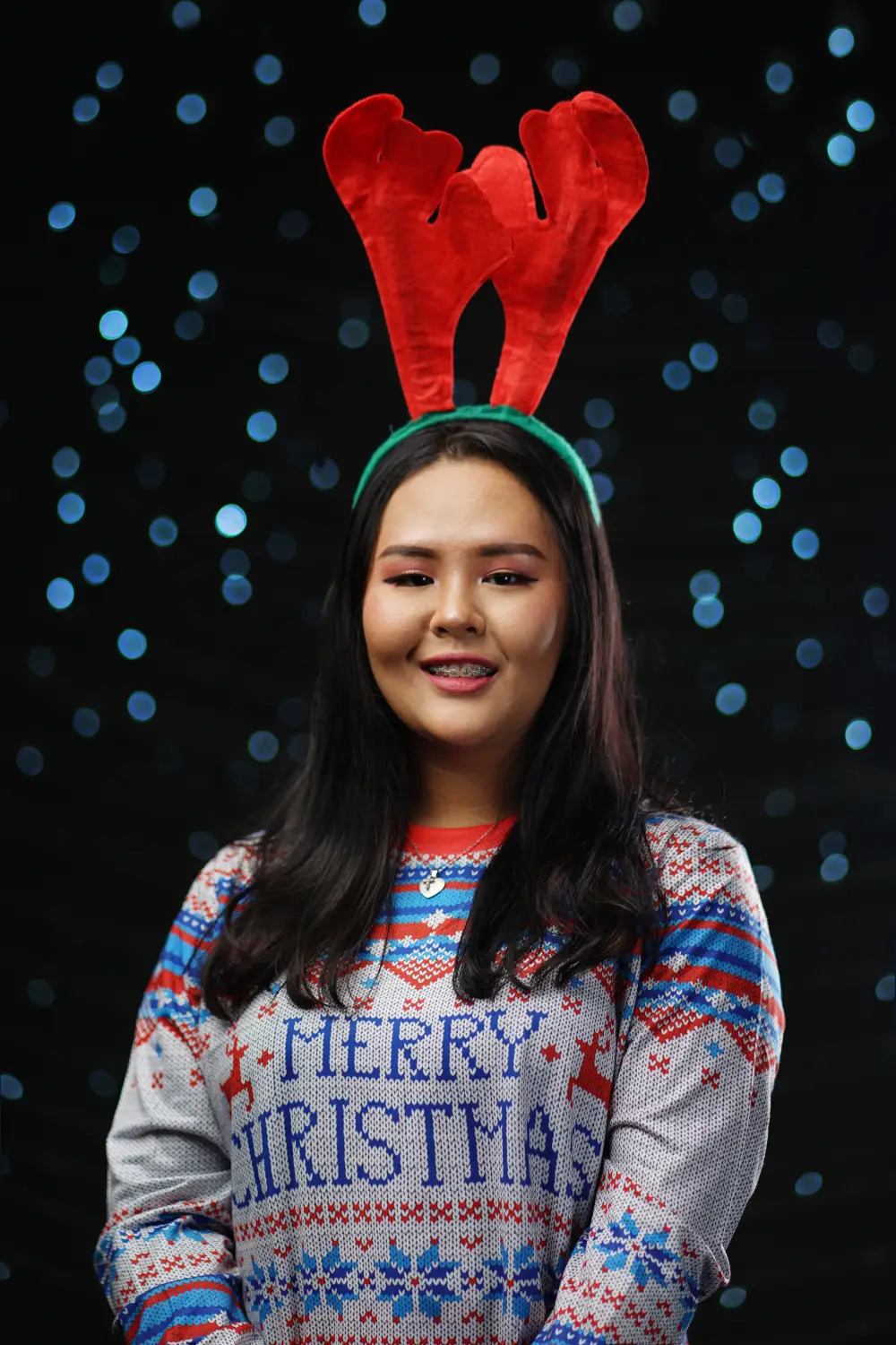 An employee wears an ugly Christmas Sweater with reindeer antlers for a virtual office holiday party
