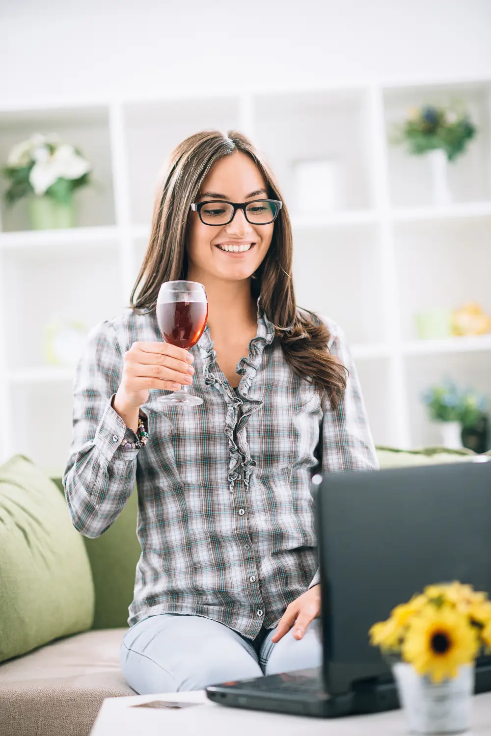 A woman holds up a drink while looking at her computer
