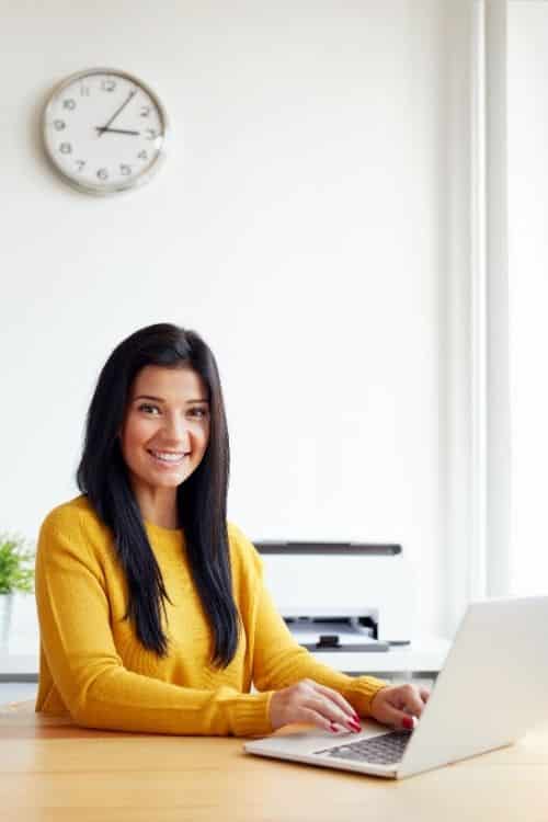 A woman wearing a yellow sweater sits in front of a computer